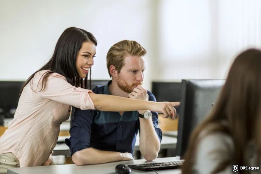 Data analyst courses: a female professor pointing to the monitor screen to guide the male student.