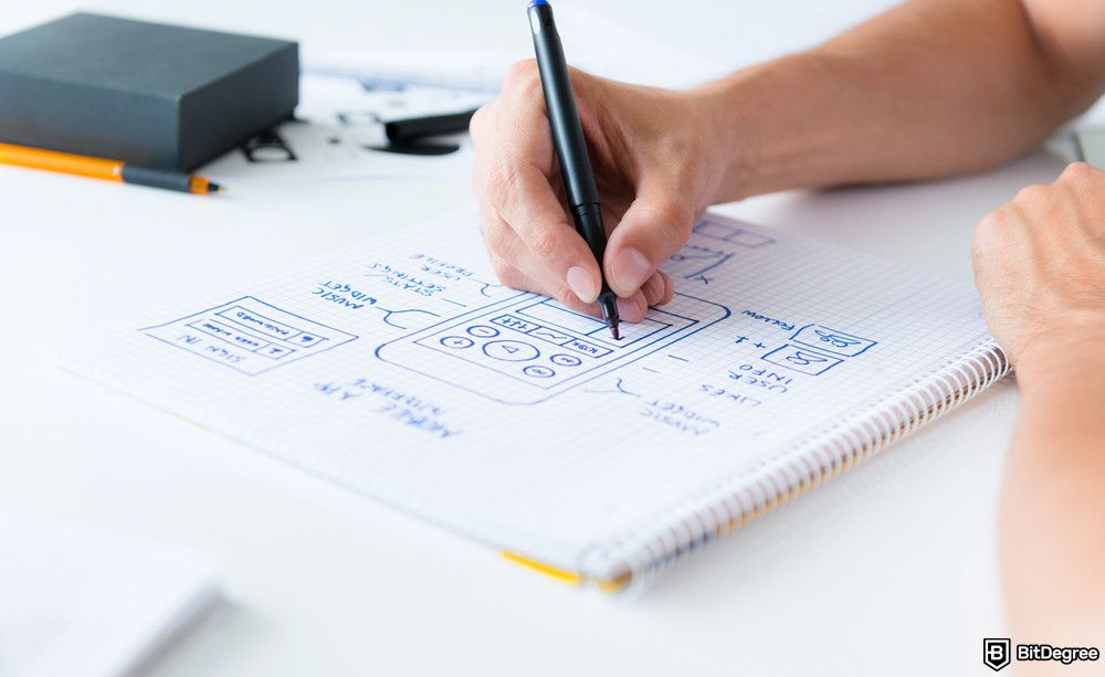 Best product management course: A close-up shot shows a person's hands using a black pen to sketch a mobile application interface.