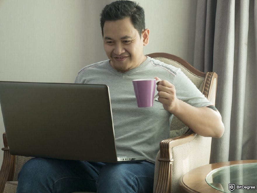eToro review: a person looking at a laptop while holding a cup, smiling.