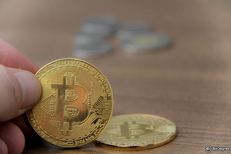 Gemini fees: a gold Bitcoin coin held in a hand, with additional coins in the background.