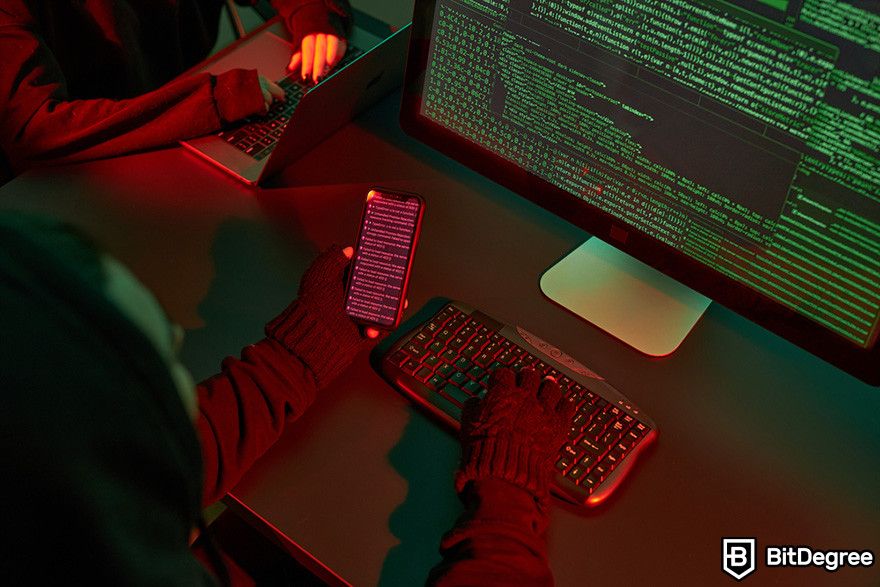 Hard token vs soft token: hackers working in a dark room, using a computer and smartphone with code on the screens.