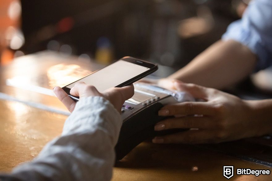 History of cryptocurrency: A customer holding a smartphone near an NFC terminal to make a mobile payment.