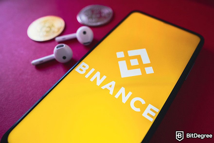 Cách vay thế chấp bằng Bitcoin: Logo Binance trên điện thoại thông minh, với tai nghe và tiền xu gần đó.