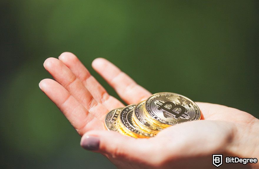 how to borrow against Bitcoin: a hand holding four BTC coins.