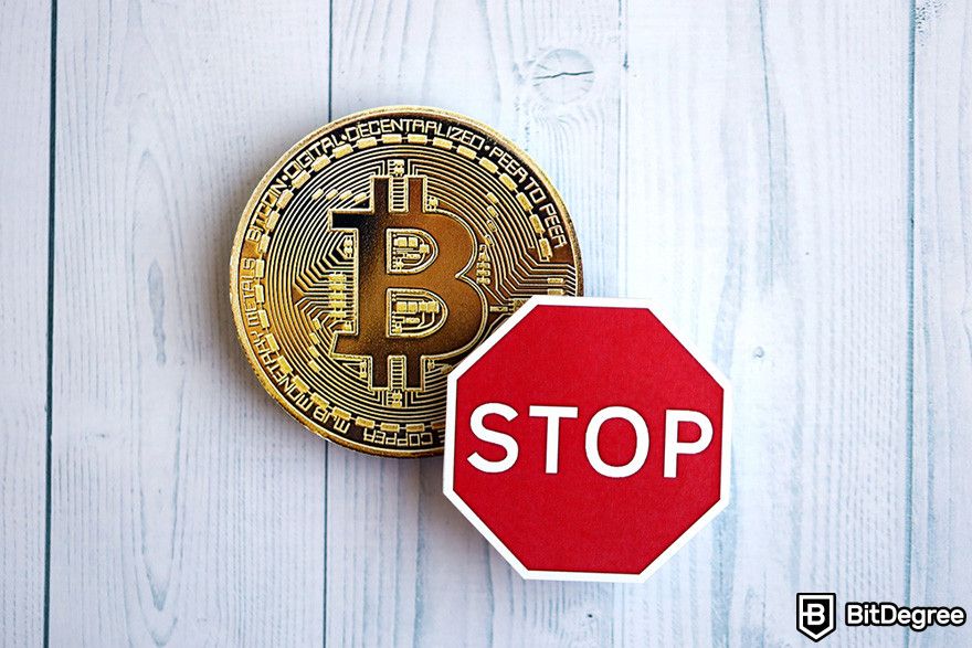 Cách vay thế chấp bằng Bitcoin: một đồng BTC và một biển báo dừng trên bề mặt gỗ màu trắng.