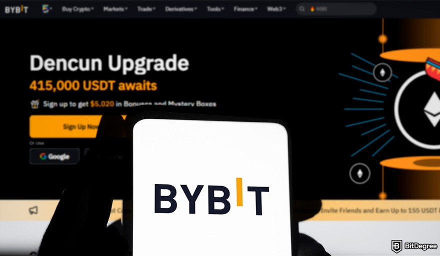 How to buy Aave: hands holding a phone showing Bybit logo in front of a screen showing Bybit homepage.