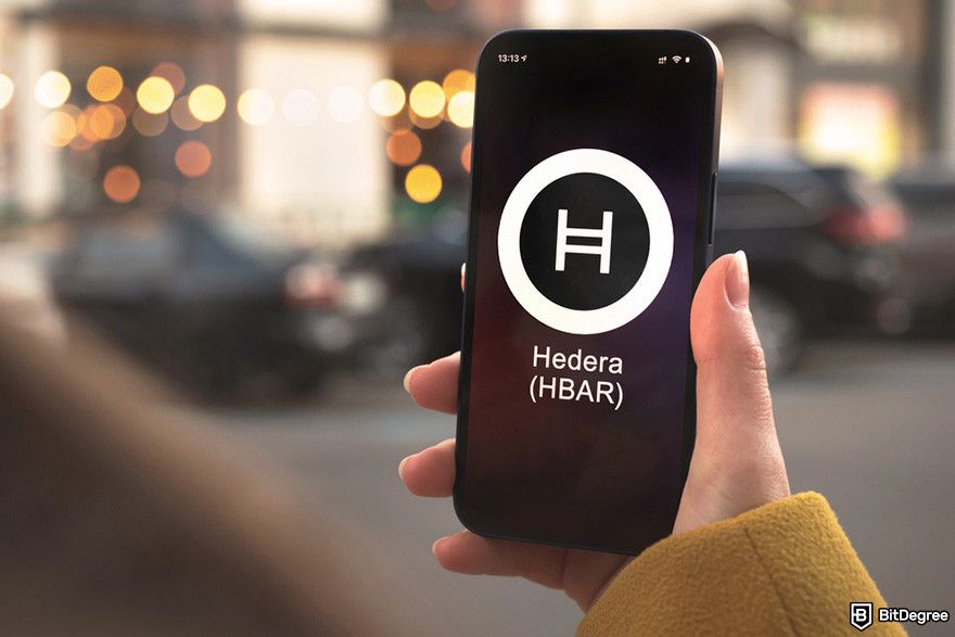 How to buy Hedera: a hand hodling a mobile phone displaying the Hedera logo.