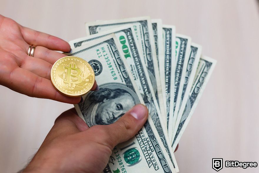 How to buy new crypto before listing: Hand holding a Bitcoin token and a fan of US dollar bills.