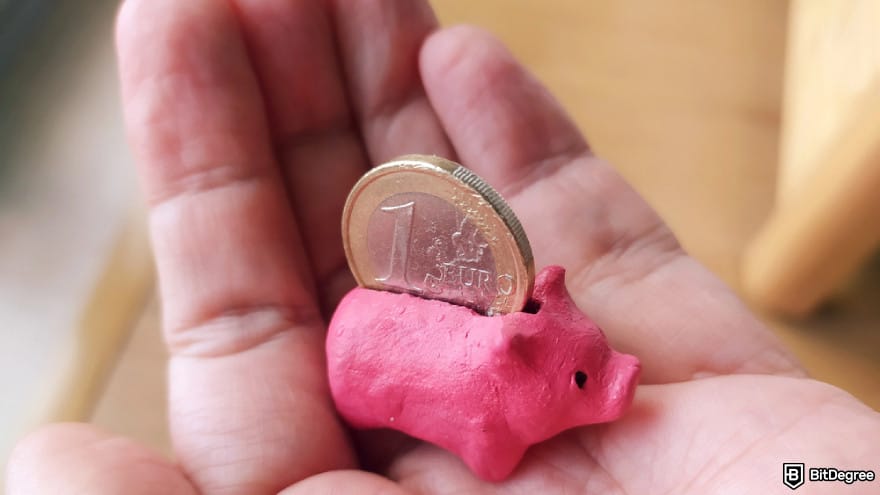 How to buy Pi Coin on Bitget: hand holding a tiny pink piggy bank with a coin.