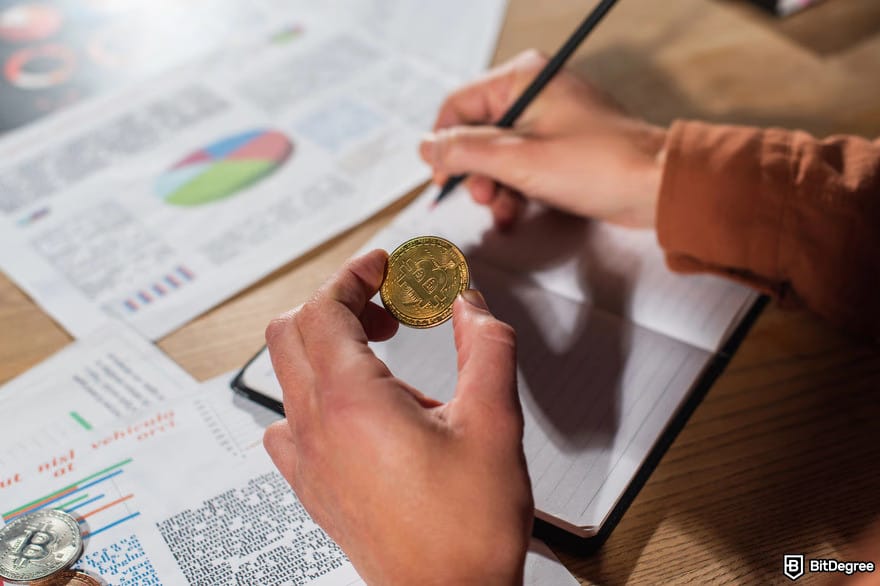 How to buy USUAL crypto: a person holding a BTC coin while writing on a notebook.