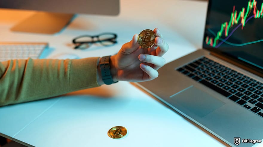 How to cash out Bitcoin: A person holding a Bitcoin with glasses and computers on a desk.