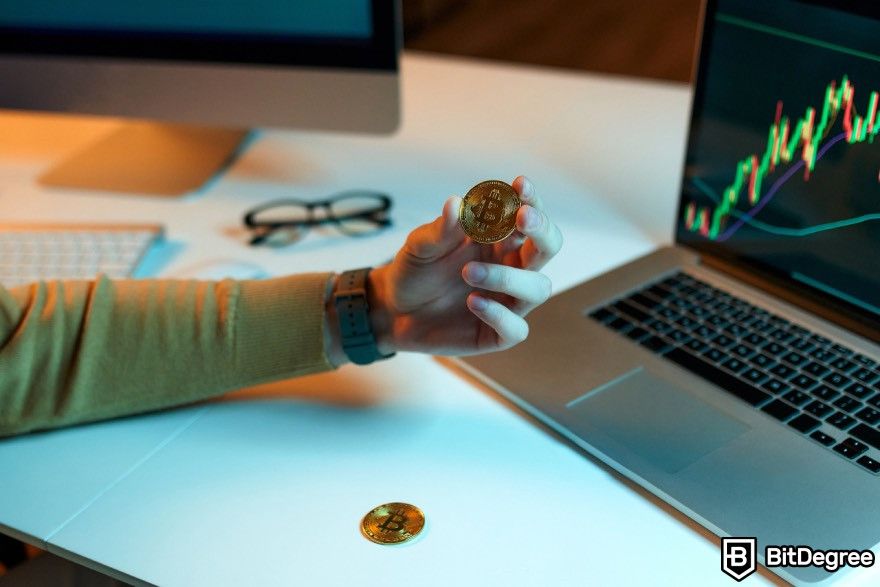 How to cash out Bitcoin: A person holding a Bitcoin with glasses and computers on a desk.