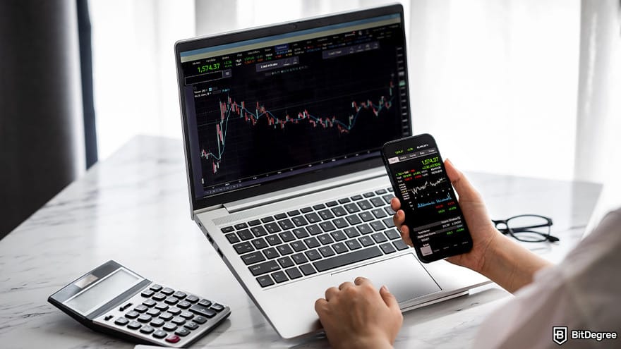 How to cash out Bitcoin: A person looking at a trading dashboard on a smartphone and a laptop with a calculator on the desk.