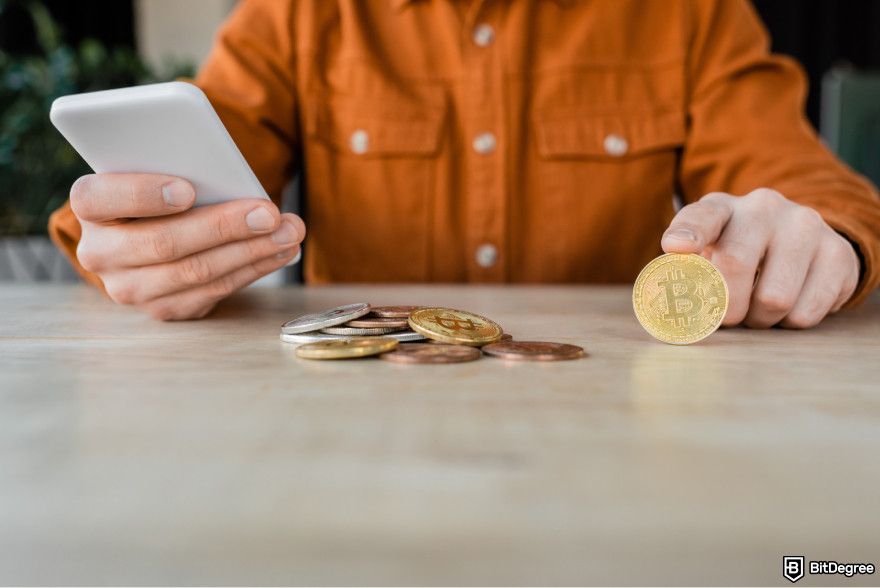 How to choose crypto trading bot: a person holding a smartphone and a Bitcoin.