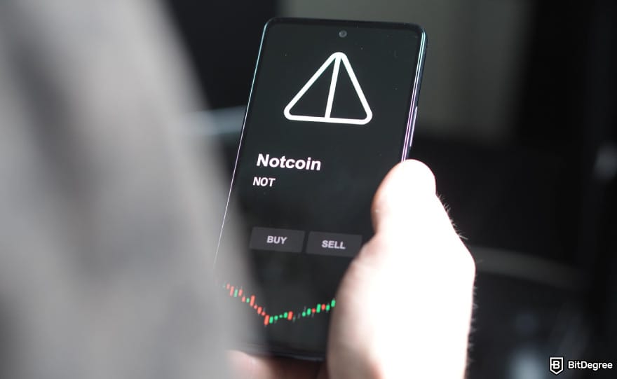 How to claim Notcoin airdrop: a person holding a phone with the Notcoin logo on it.