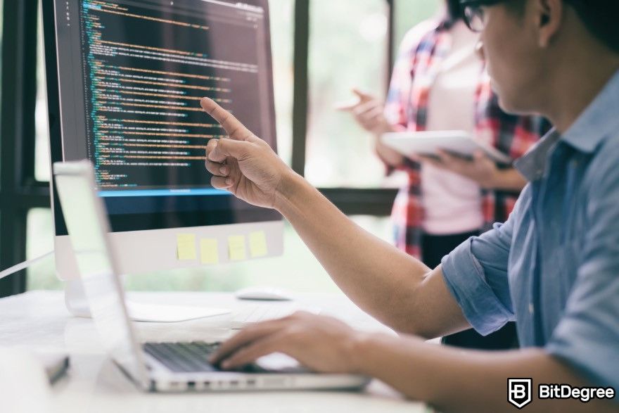 How to code for beginners: A man pointing at a monitor with code displayed on it.