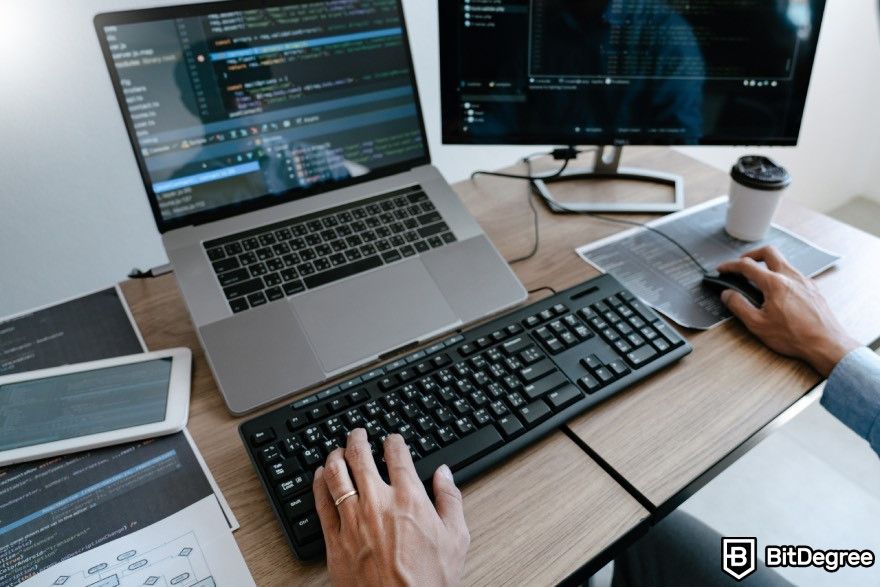 How to code for beginners: A person typing on a laptop with a monitor placed on a desk.