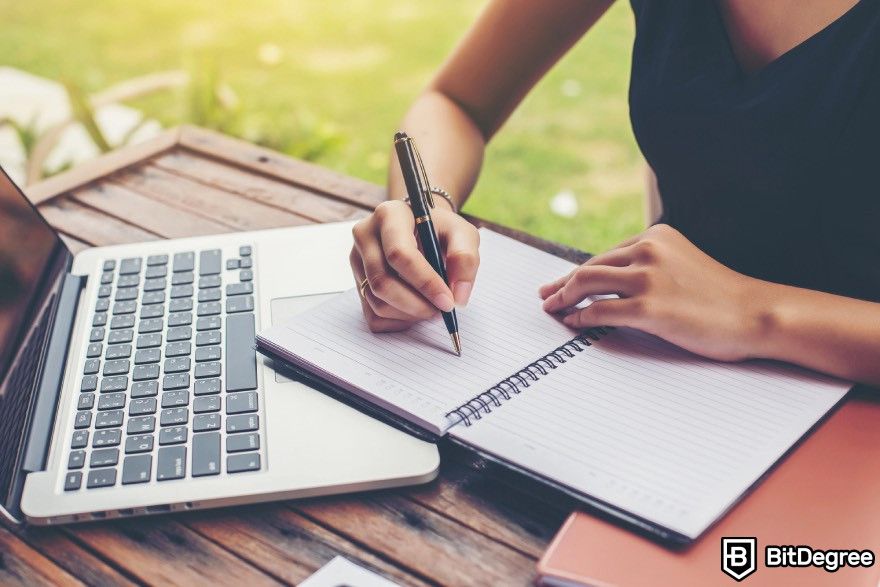 How to code for beginners: A person writing in a notebook with a laptop placed beside them.