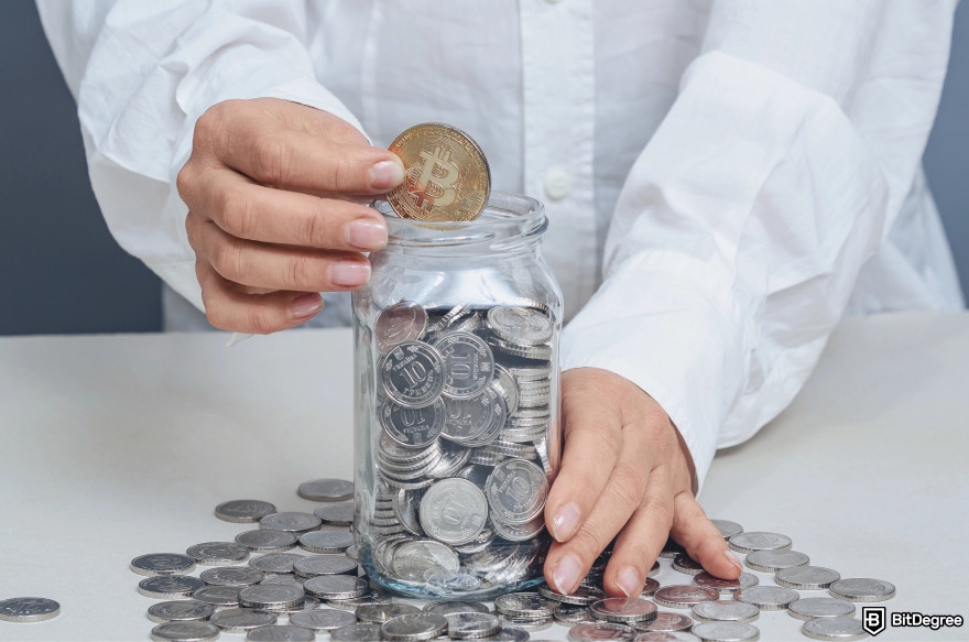 How to get crypto airdrops: a person putting a Bitcoin in a jar.