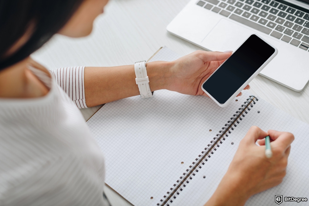 How to get free money online: a woman is writing on a notebook while holding her phone.