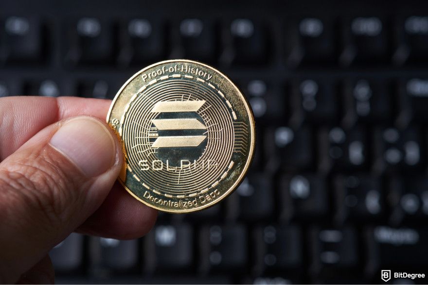 How to get Phantom airdrop: a person holding a Solana coin in front of a keyboard.