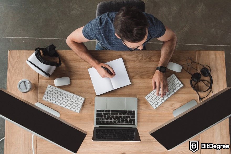 How to make a video game: A person writing in a notebook and typing on a keyboard.