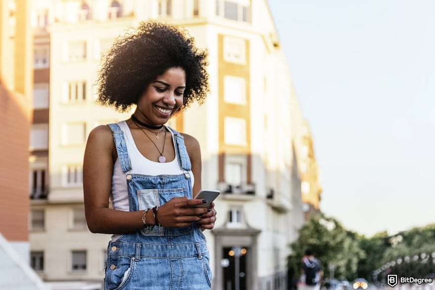 How to make a money online in Nigeria: a woman smiling while looking at her phone in the city.
