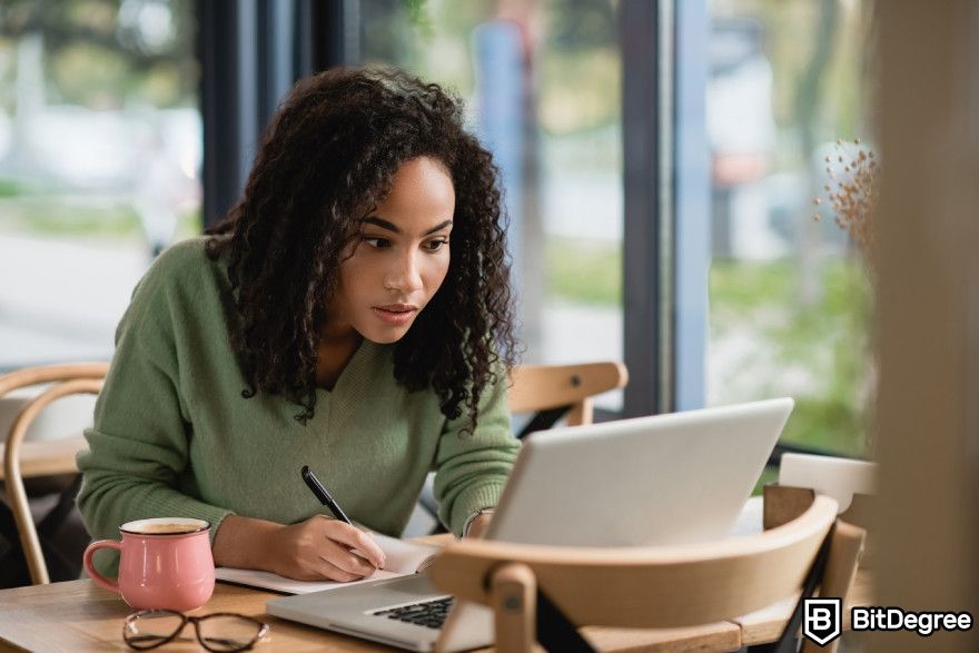 How to make money with AI: Woman learning and writing notes on a laptop.