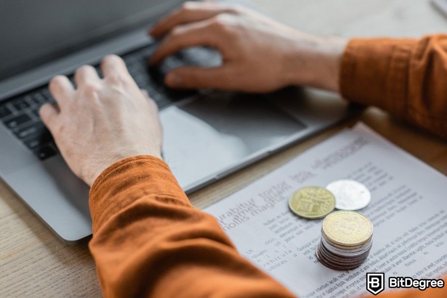 How to mine cryptocurrency: A person is typing on a laptop with coins placed on a paper.