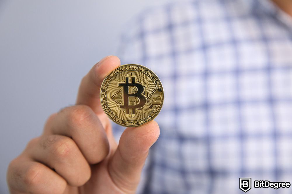 How to pay with Bitcoin: a man holding a Bitcoin physical coin.