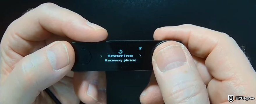 How to recover Ledger: a pair of hands holding a Ledger wallet with the Restore menu displayed.