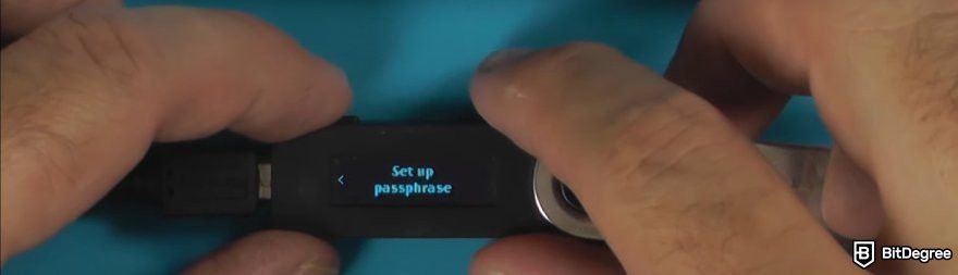 How to recover Ledger: a hand holding a Ledger device with Set up passphrase displayed.