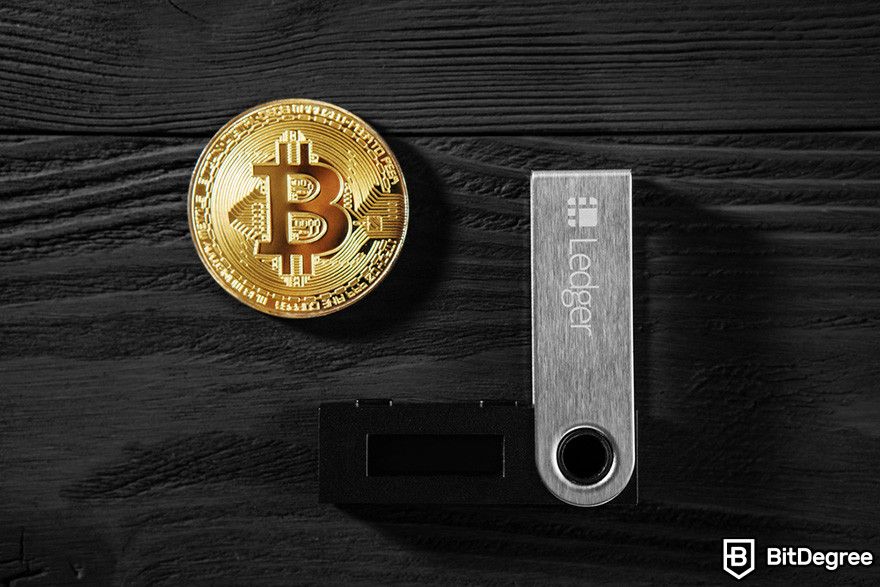 How to sell crypto from cold wallet: a gold BTC coin and a Ledger hardware wallet on a dark wooden surface.