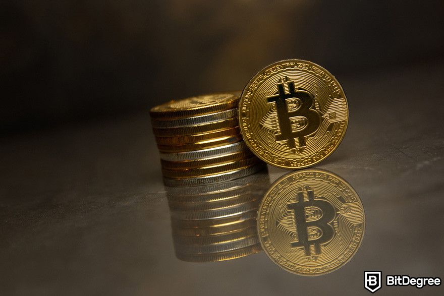 How to send Bitcoin to another wallet: a stack of gold BTC coins on a reflective surface.