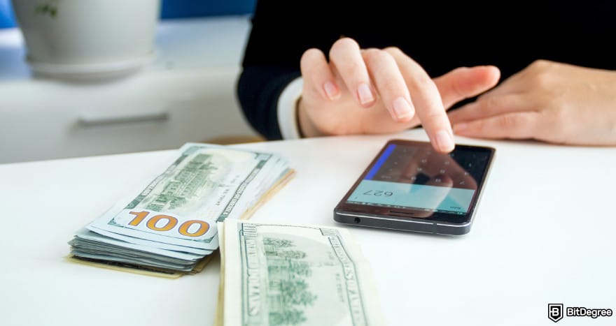 How to send money to someone without a bank account: woman with a phone next to dollar bills to illustrate sending money.
