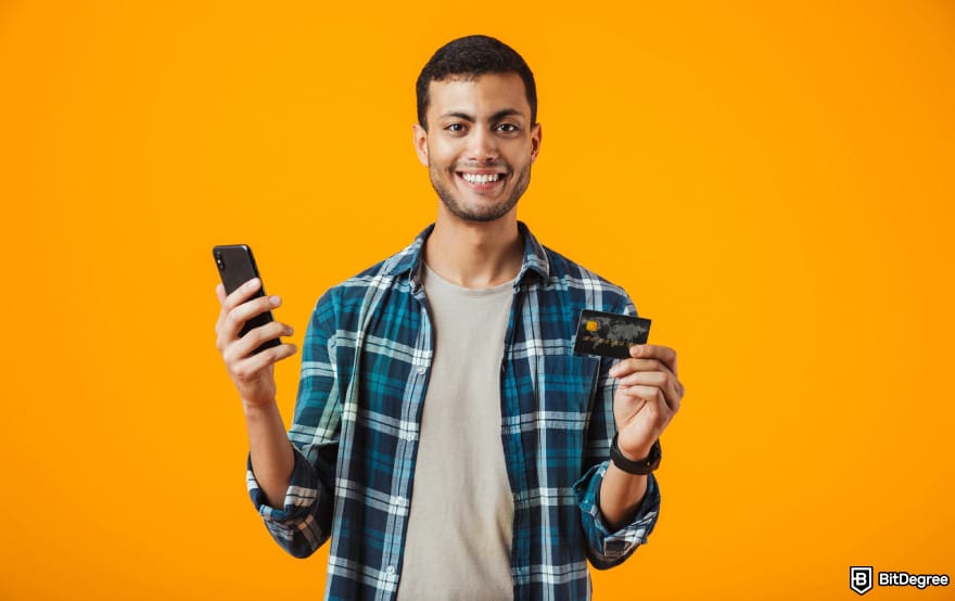 How to send money with debit card: man holding phone and debit card to illustrate sending money online with a debit card.