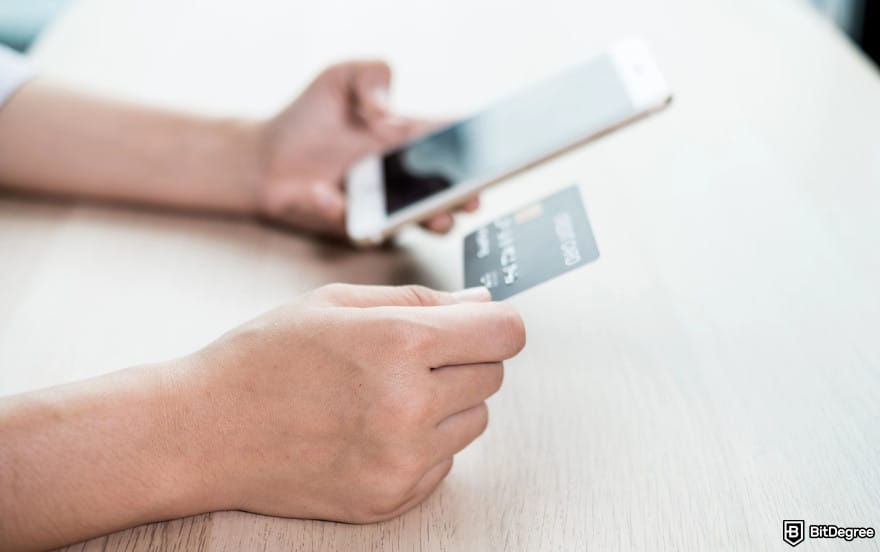 How to send money with debit card: person holding card and a phone to illustrate online debit cards.
