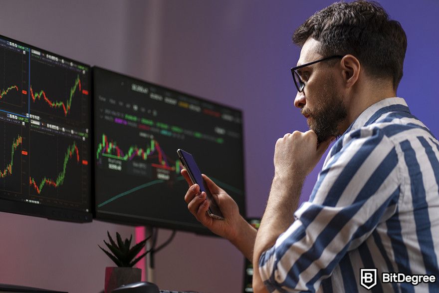 How to short crypto: Man checking crypto charts on screens and a phone.