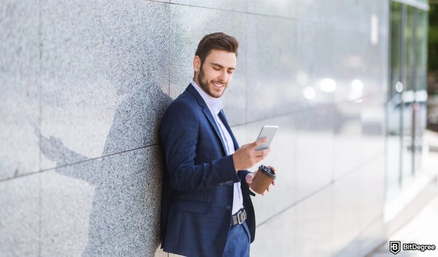 How to trade US stocks for beginners: a person looking at a mobile phone smiling. How to trade US stocks for beginners: a person looking at a mobile phone smiling.