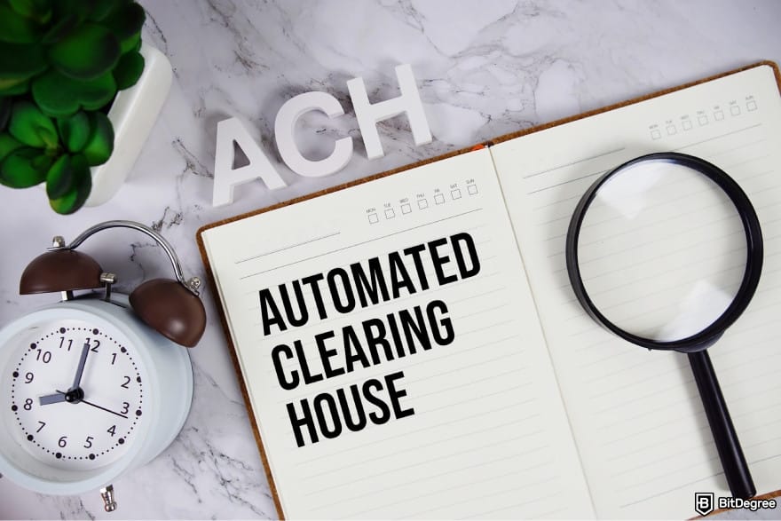 How to transfer money from bank account: a notebook with a magnifying glass on top with the words AUTOMATED CLEARING HOUSE.