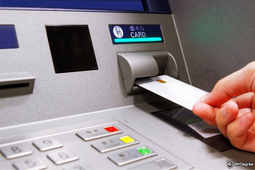 How to transfer money from bank account: a person inserting a card into an ATM.