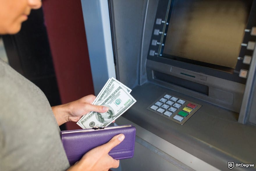 How to transfer money from one bank to another: a person holding money in front of an ATM.