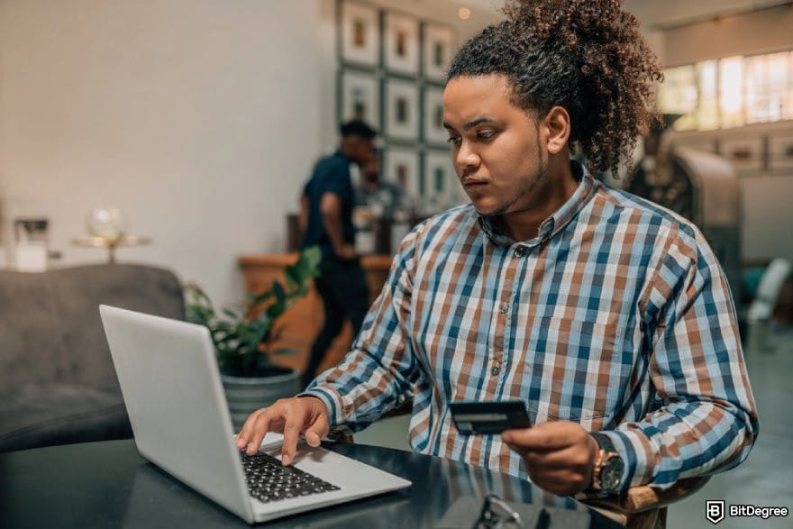 How to transfer money from one bank to another: a person holding a debit card while using a laptop.