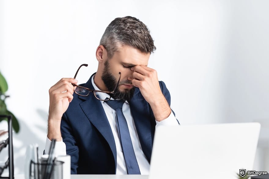 How to transfer money from Venmo to bank: an overworked businessman holding eyeglasses and looking frustrated in front of his laptop.