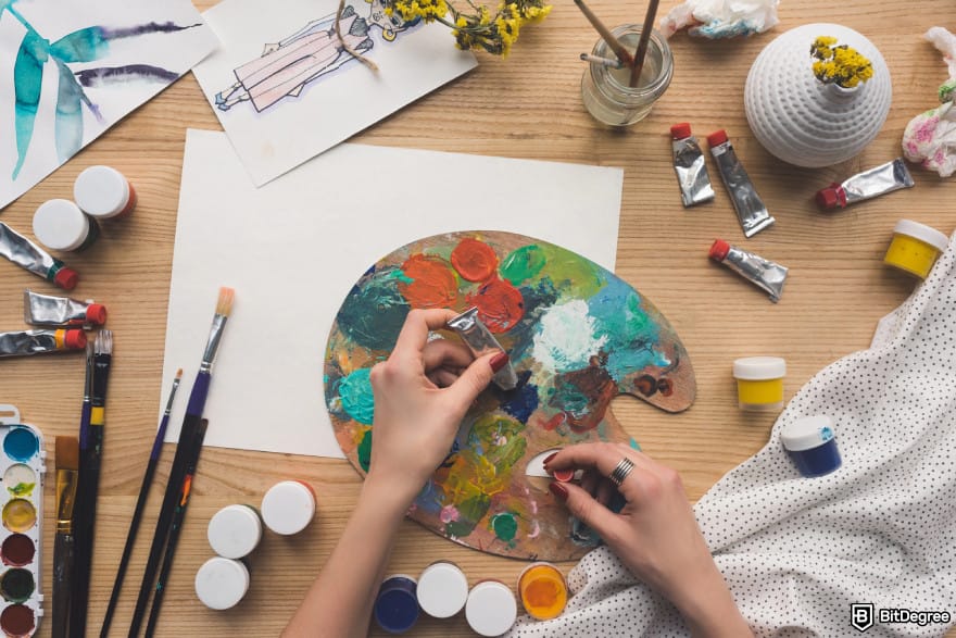 How to use DALL-E: a pair of hands pouring paint into a palette surrounded by painting supplies.
