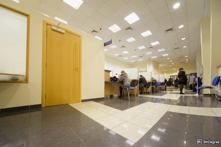 How to wire money: a bank branch with people in every counter and a woman standing up on the side.