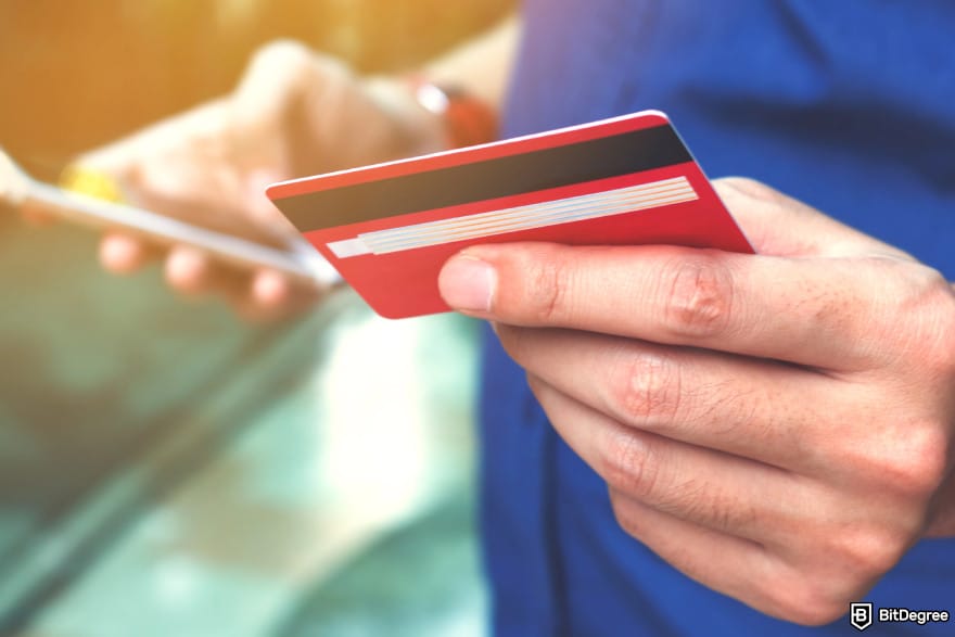 How to wire money: a man holding a debit card while looking at his phone in the other.