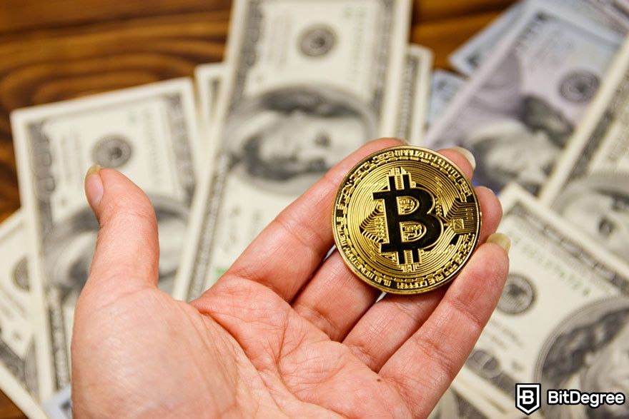 How to withdraw from Coinbase: A hand holding a Bitcoin token with hundred dollar bills in the background.