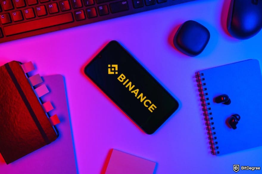 How to withdraw money from Binance: a phone displaying the Binance logo surrounded by notebooks.