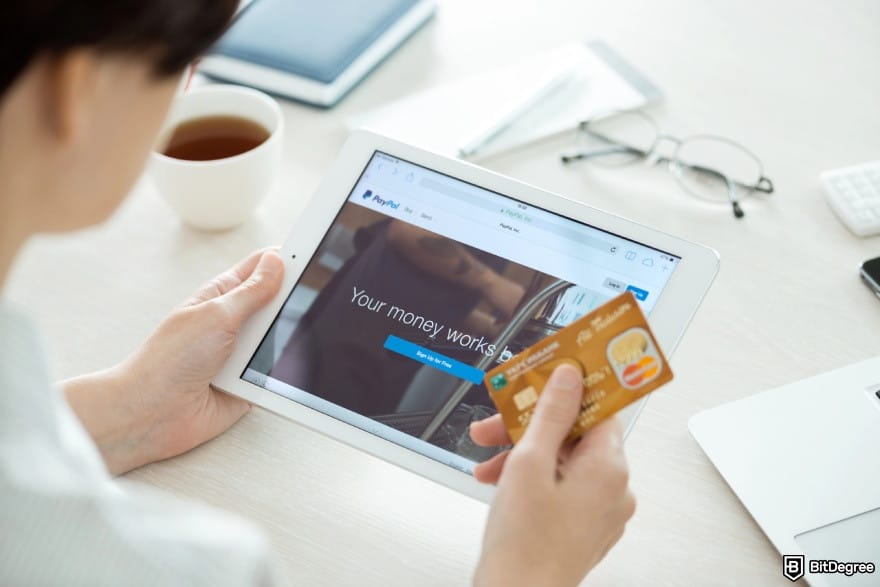 How to withdraw money from PayPal: a person opening PayPal on their tablet while holding a card.